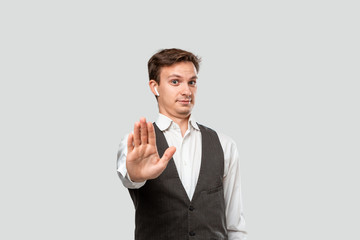 Confindent handsome man in a white shirt and grey vest expressing Stop gesture isolated over grey background. Being fed up