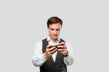 Handsome young man in a white shirt and grey vest playing game on a smartphone.