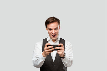 Handsome young man in a white shirt and grey vest playing game on a smartphone.