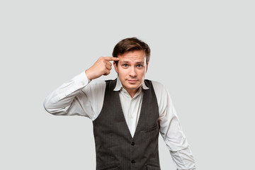 Young businessman in a white shirt and grey vest is at lost shrugging his shoulders isolated over grey background.