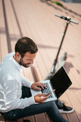 Young businessman outdoors using phone and laptop