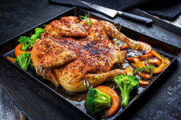 Barbecue Hühnchen al Mattone mit Chili, Kürbis und Broccoli als closeup auf einem alten Metall...