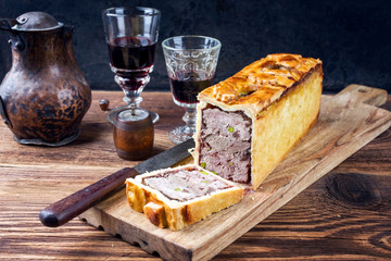 Traditional French Pate en croute with goose meat and liver as closeup with red wine on a wooden board