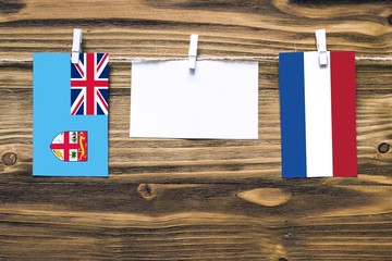Hanging flags of Fiji and Netherlands attached to rope with clothes pins with copy space on white note paper on wooden background.Diplomatic relations between countries.