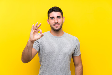 Young handsome man over isolated yellow background showing an ok sign with fingers