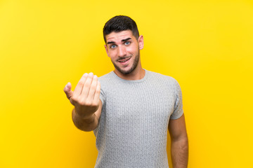 Young handsome man over isolated yellow background inviting to come