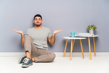 Young handsome man sitting on the floor having doubts with confuse face expression