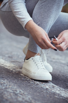 girl squatted down to tie shoelaces on white sneakers on asphalt road, autumn sport concept outdoors © fantom_rd