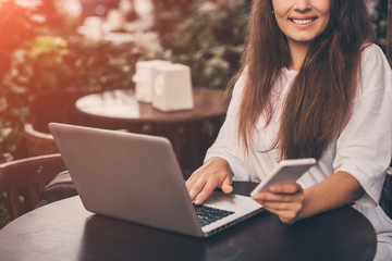 Beautiful woman work on laptop and using phone sitting in street cafe.