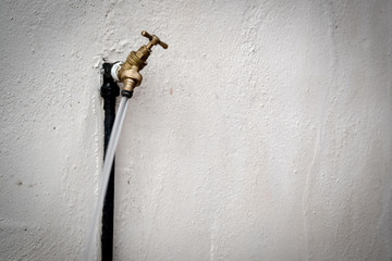 Isolated view of a running outside brass tap. Taken using a slow shutter the water forms a blur against the outside wall. Used for garden irrigation and other duties.