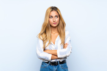 Young blonde woman over isolated blue background with confuse face expression