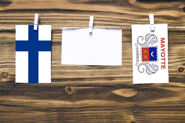 Hanging flags of Finland and Mayotte attached to rope with clothes pins with copy space on white note paper on wooden background.Diplomatic relations between countries.