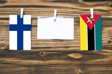 Hanging flags of Finland and Mozambique attached to rope with clothes pins with copy space on white note paper on wooden background.Diplomatic relations between countries.