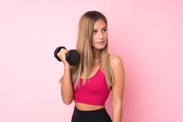 Young sport blonde woman over isolated pink background making weightlifting with kettlebell