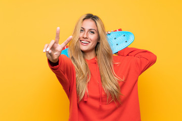 Young skater woman making victory gesture over isolated yellow background