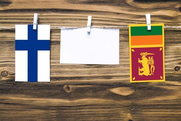 Hanging flags of Finland and Sri Lanka attached to rope with clothes pins with copy space on white note paper on wooden background.Diplomatic relations between countries.