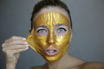 Beautiful girl peeling off golden face mask. Skin treatment.