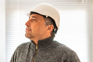 Profile portrait of a serious civil engineer or factory worker wearing a white helmet