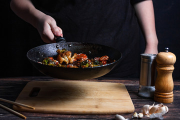 Chef at work. Hand holds a hot pan with fried vegetables, broccoli, cauliflower, carrots.