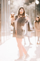 Happy young woman walking in the street with dog and shopping bags