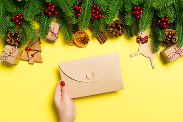 Top view of woman holding an envelope on yellow background made of holiday decorations. Christmas time concept