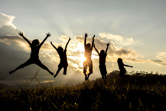 Silhouette group of happy children jumping playing on mountain at sunset, summer time