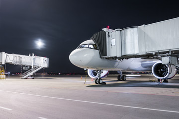 A white passenger jet plane stands at the air bridge connected to an external power supply on an...