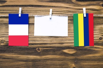 Hanging flags of France and Mauritius attached to rope with clothes pins with copy space on white note paper on wooden background.Diplomatic relations between countries.