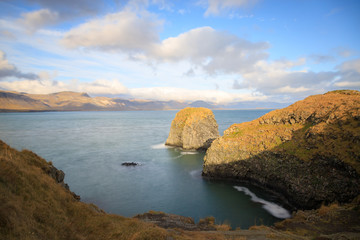 West coast sea cliffs of Snaefellsnes Peninsula on Iceland in long exposure photo. Pure blue water with high cliffs above sea. Beautiful colourful scenic view of basalt rock reef..