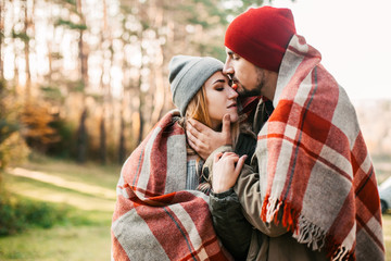 Couple huggings travelers covered with plaid in the forest. Concept of trekking, adventure and seasonal vacation.