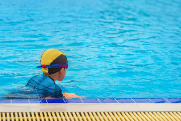 5 years old Lonely boy warm up with orange swimming kickboard before learning to swim in the blue...