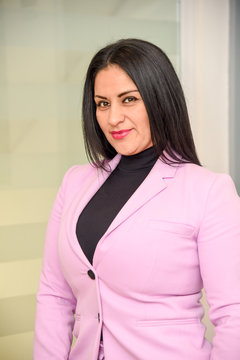 Latin woman executive businesswoman with black hair and pink suit, Latin woman, business woman, smiling, black eyes, long hair, executive, wearing phone, high heels