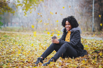 Dark-skinned woman dressed in casual clothes holding cup of hot drink, enjoying coffee or tea