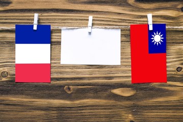 Hanging flags of France and Taiwan attached to rope with clothes pins with copy space on white note paper on wooden background.Diplomatic relations between countries.