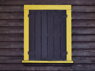 Yellow framed window with wooden storm shutters on the exterior wall of a cabin.