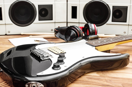 Guitar with drumsticks and audio equipment on wooden desk.