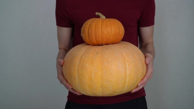 Young man holds two pumpkins in his hands close-up