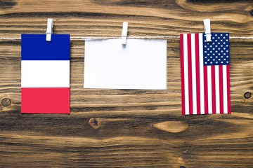 Hanging flags of France and United States attached to rope with clothes pins with copy space on white note paper on wooden background.Diplomatic relations between countries.