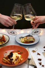 Festive holiday table with pork belly roast, mashed potatoes and roasted vegetables. Unrecognizable people cheering with white wine. 