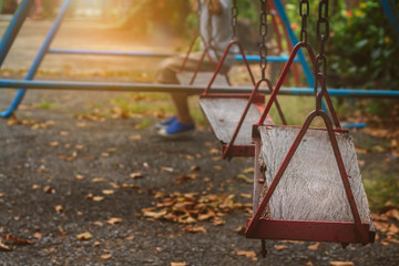 Blurred alone boy sitting on old wooden garden swings in abandoned playground with sunset lighting...