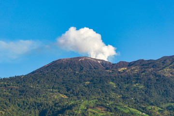 Volcano erupting smoke against bright blue sky