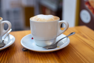 White cup with cappucino coffee with whipped hot milk