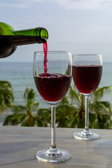 Waiter pouring red wine in glasses in lounge bar with sea view and palm trees