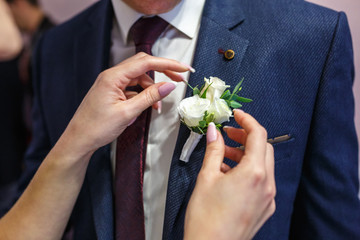 bride puts groom on boutonniere from pink and whote rose on wedding day - obrazy, fototapety, plakaty