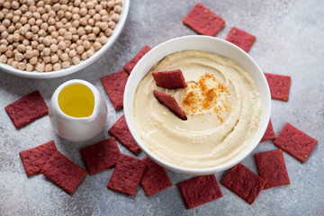 Hummus served in a white bowl with beetroot crackers, studio shot on a beige stone surface, elevated view