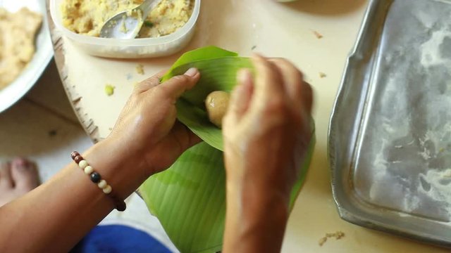 Asian woman making a Thai dessert by covering a flour ball with banana leaf before put to steaming pot.