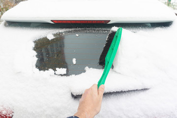 Man cleaning car from snow with brush. Snow-covered car windshield. parked car covered with snow during snowing in winter time.