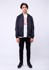 Young man in jeans, black bomber jacket on white background.