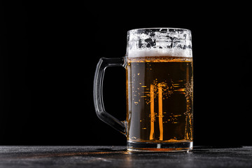 Glass mug filled with fresh beer with foam against black background.