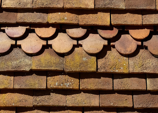 Close up image of the textured detail, antique clay tiles on roof of a Victorian property. Weathered by the seasons. Geometric patterns, sunlit with shadows, layered depth. England